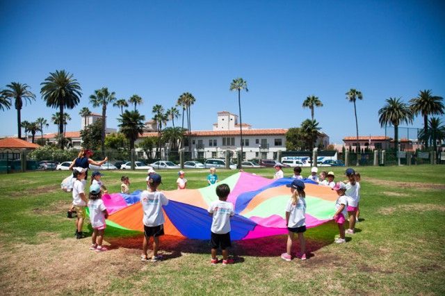 A group of children are playing with a parachute in a field.