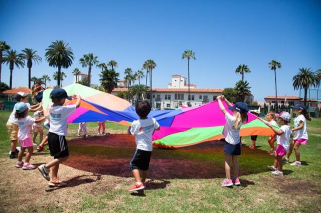 A group of children are playing with a colorful parachute in a field.