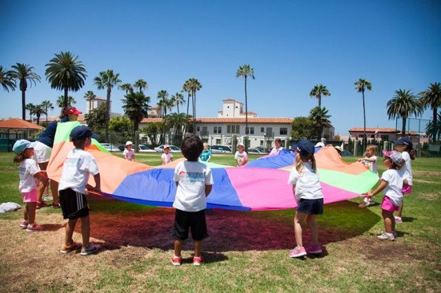 A group of children are holding a colorful parachute in a field.