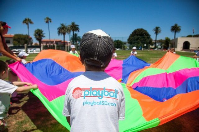 A boy wearing a playball shirt is holding a colorful parachute
