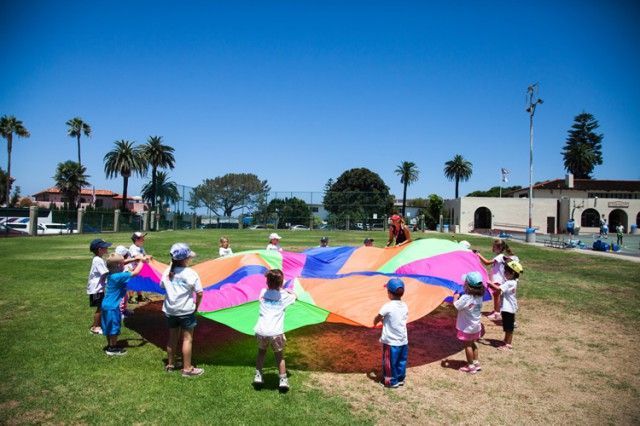 A group of children are playing with a colorful parachute in a field.