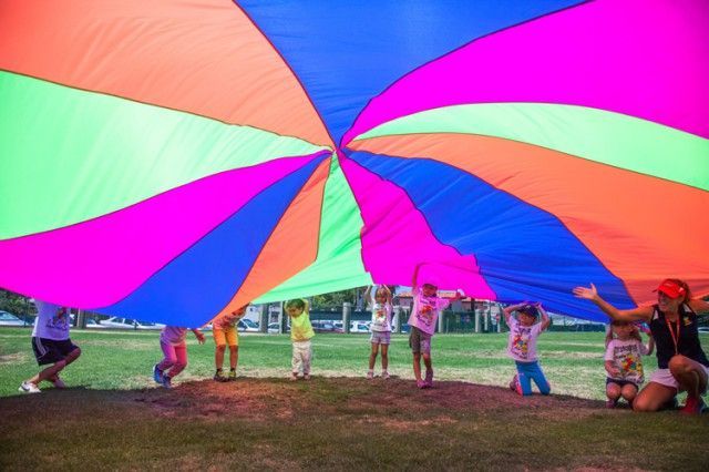 A group of children are playing with a colorful parachute.