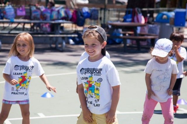 A group of children wearing playbook shirts are standing on a court