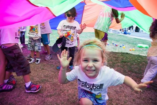 A little girl is playing under a colorful parachute.