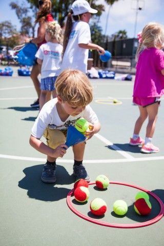 A group of children are playing with tennis balls on a court.