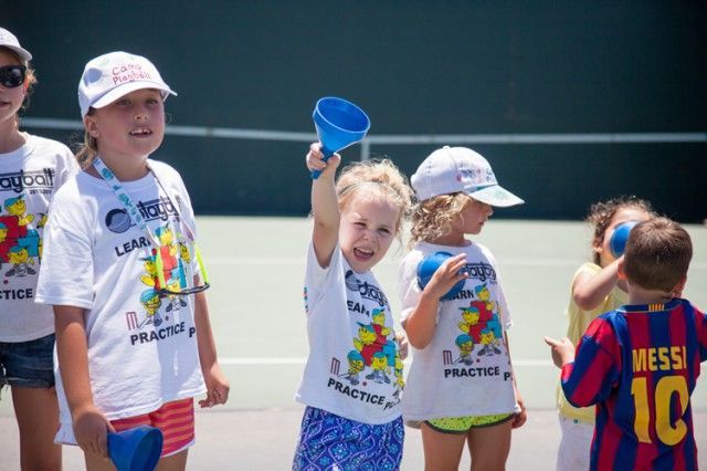 A group of young children are standing on a tennis court.