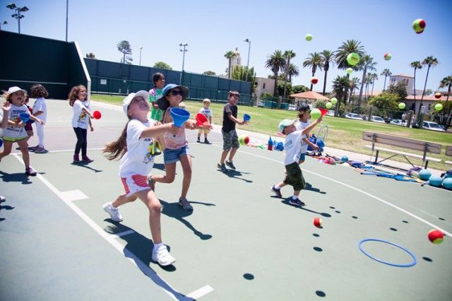 A group of children are playing with tennis balls on a tennis court.
