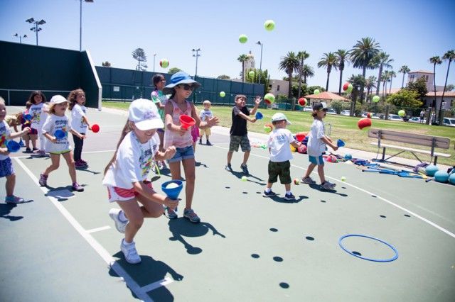 A group of children are playing with tennis balls on a tennis court