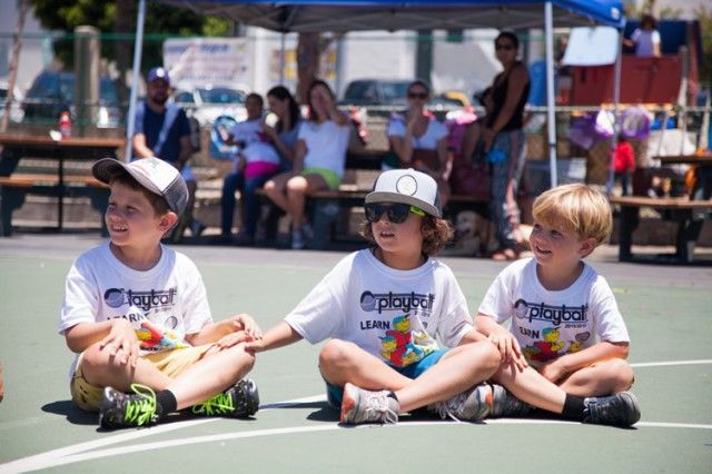 Three young boys are sitting on a basketball court with their legs crossed.