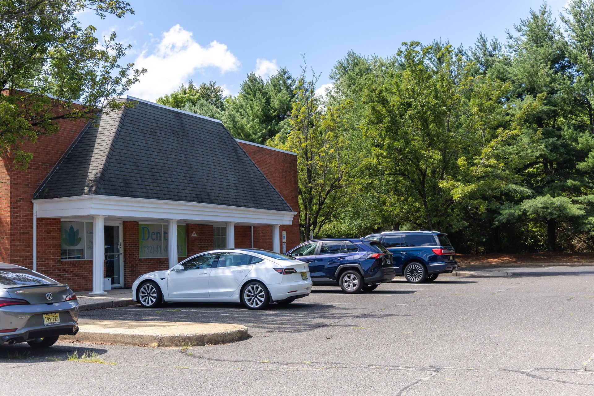 Exterior view of a brick building with parked cars, surrounded by trees under a blue sky.