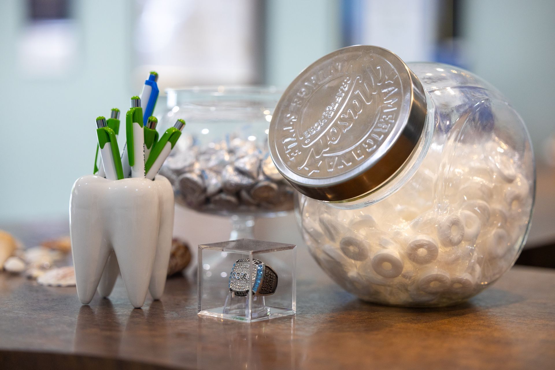 Tooth-shaped pen holder with pens, ring in a box, a candy jar, and a jar with candies on a table.