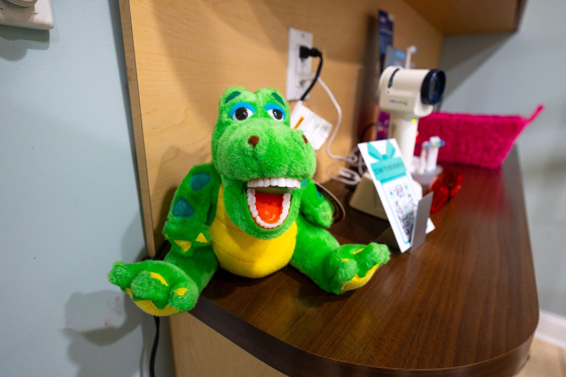 Green plush alligator with open mouth, displaying teeth, on a wooden shelf in a medical setting.