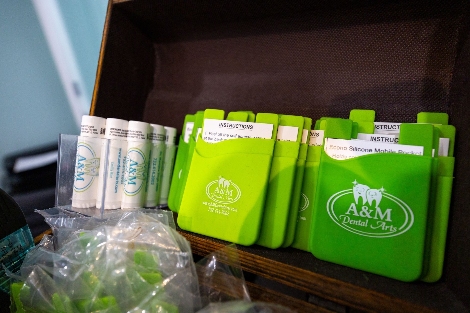 A wooden box holding stacks of green cardholders and lip balms, all branded 