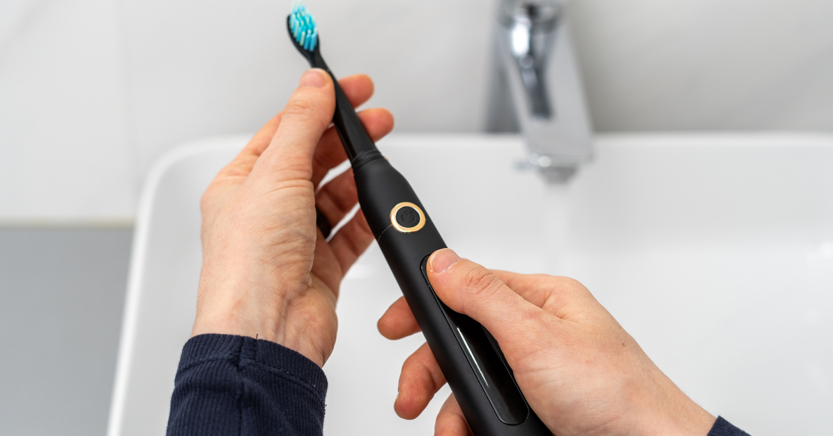 Person holds black electric toothbrush over a white sink.