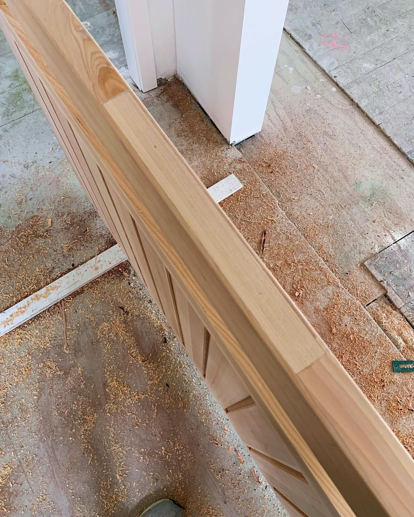 A close-up of a new wooden door edge installed in a frame, surrounded by sawdust on the floor.