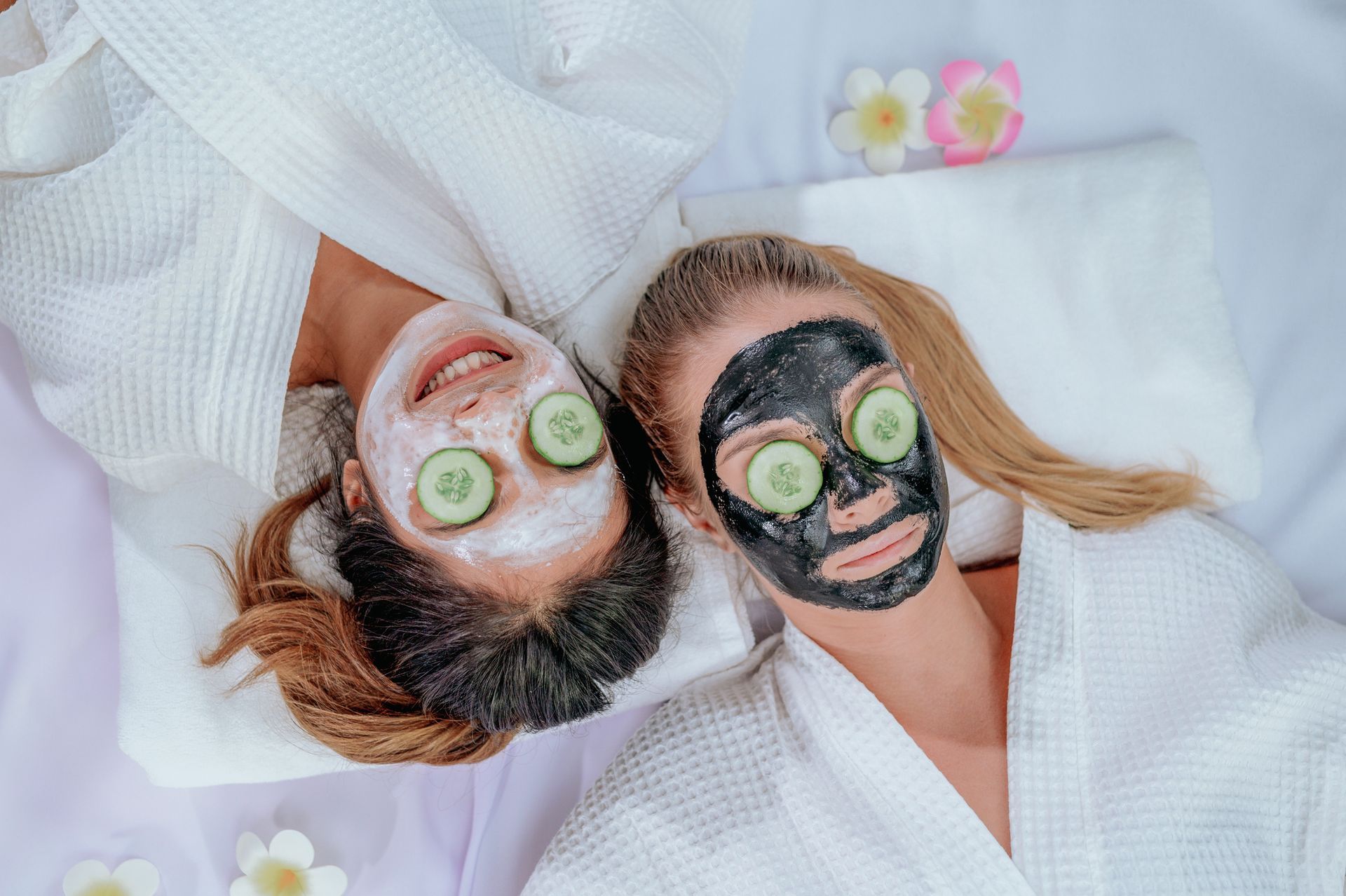 Two women are laying on a bed with masks on their faces.