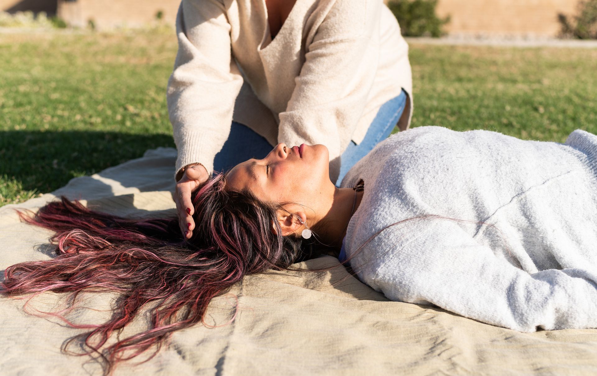 A woman is laying on a blanket in the grass getting a massage from another woman.