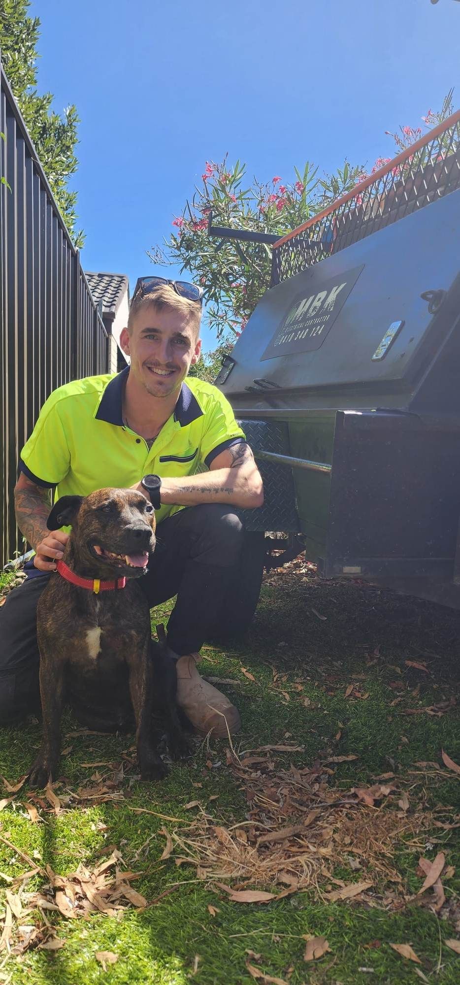 Man with dog in a backyard. Man kneeling, wearing a neon shirt, dog has a red collar.