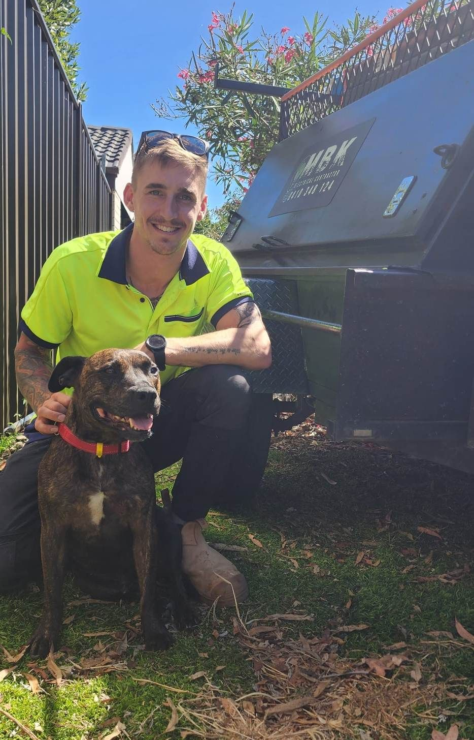 Man in Neon Shirt With Dog, Kneeling by a Dumpster — MBK Electrical Contractor  In Blayney, NSW