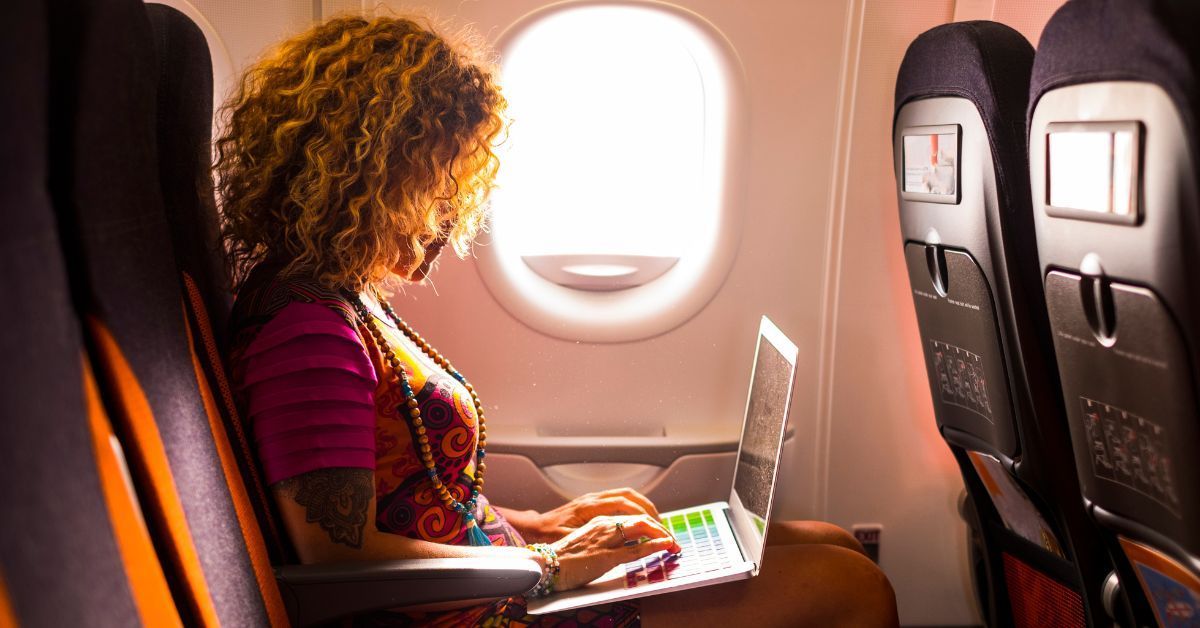 A woman is sitting on an airplane using a laptop computer.