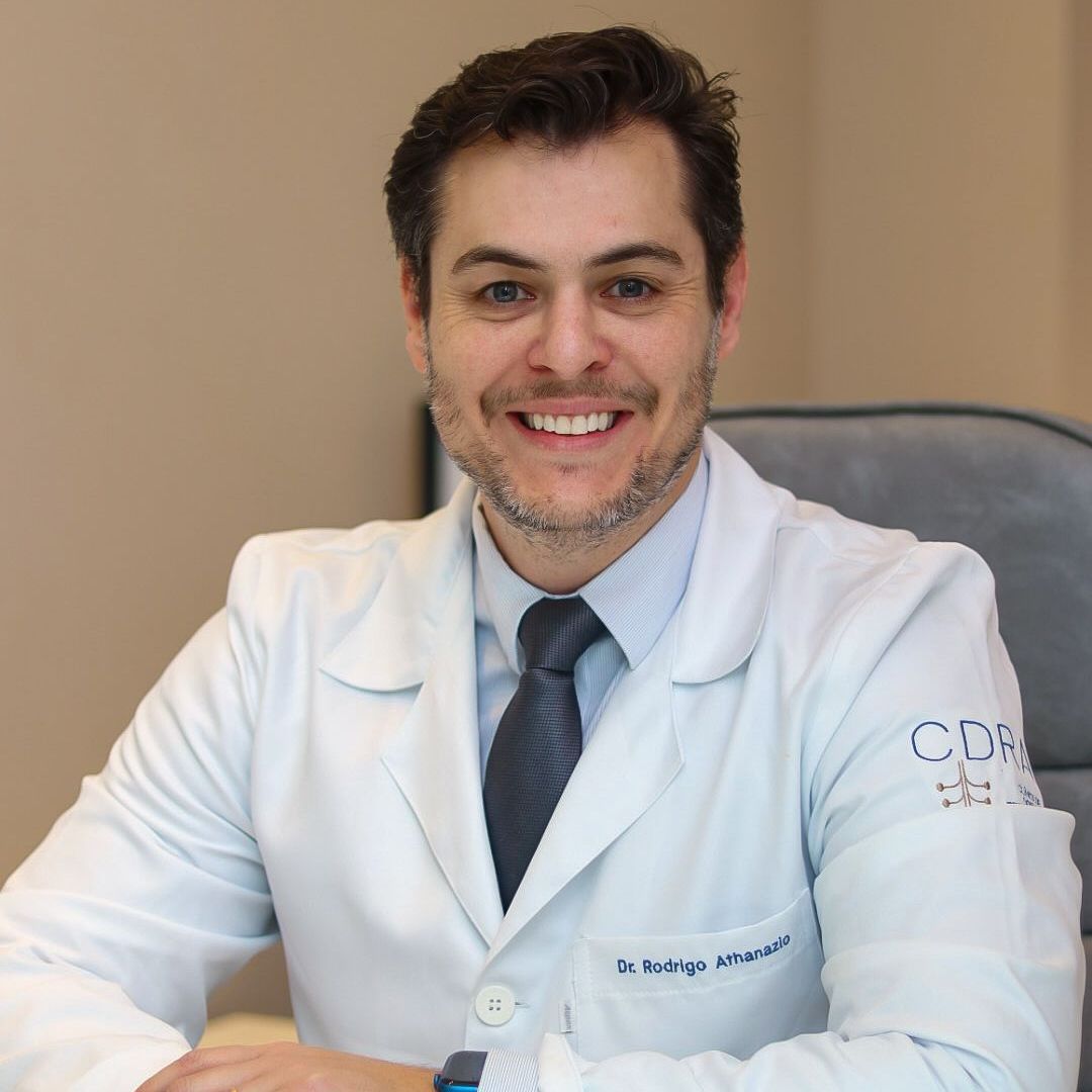 Um homem com jaleco está sentado em uma mesa em frente a um computador.