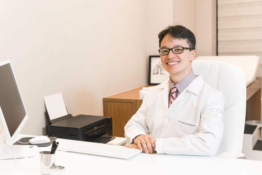 Um médico está sentado em uma mesa em frente a um computador.