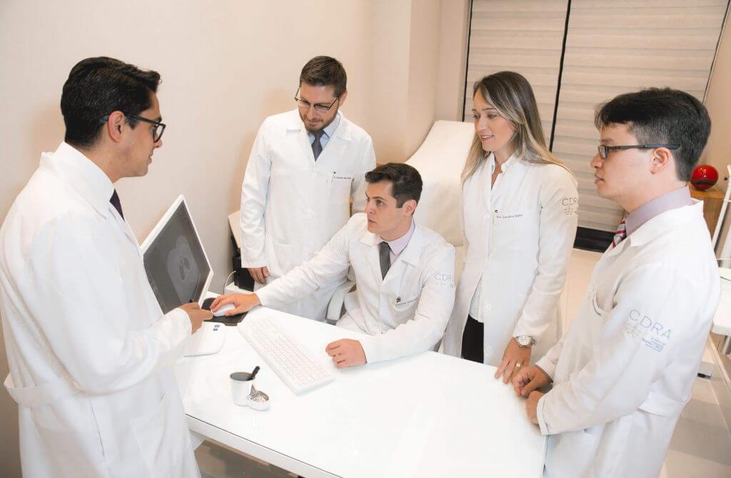 Um grupo de médicos está em volta de uma mesa olhando para um laptop.