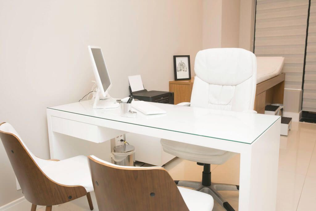 Consultório médico com mesa, cadeiras e computador.