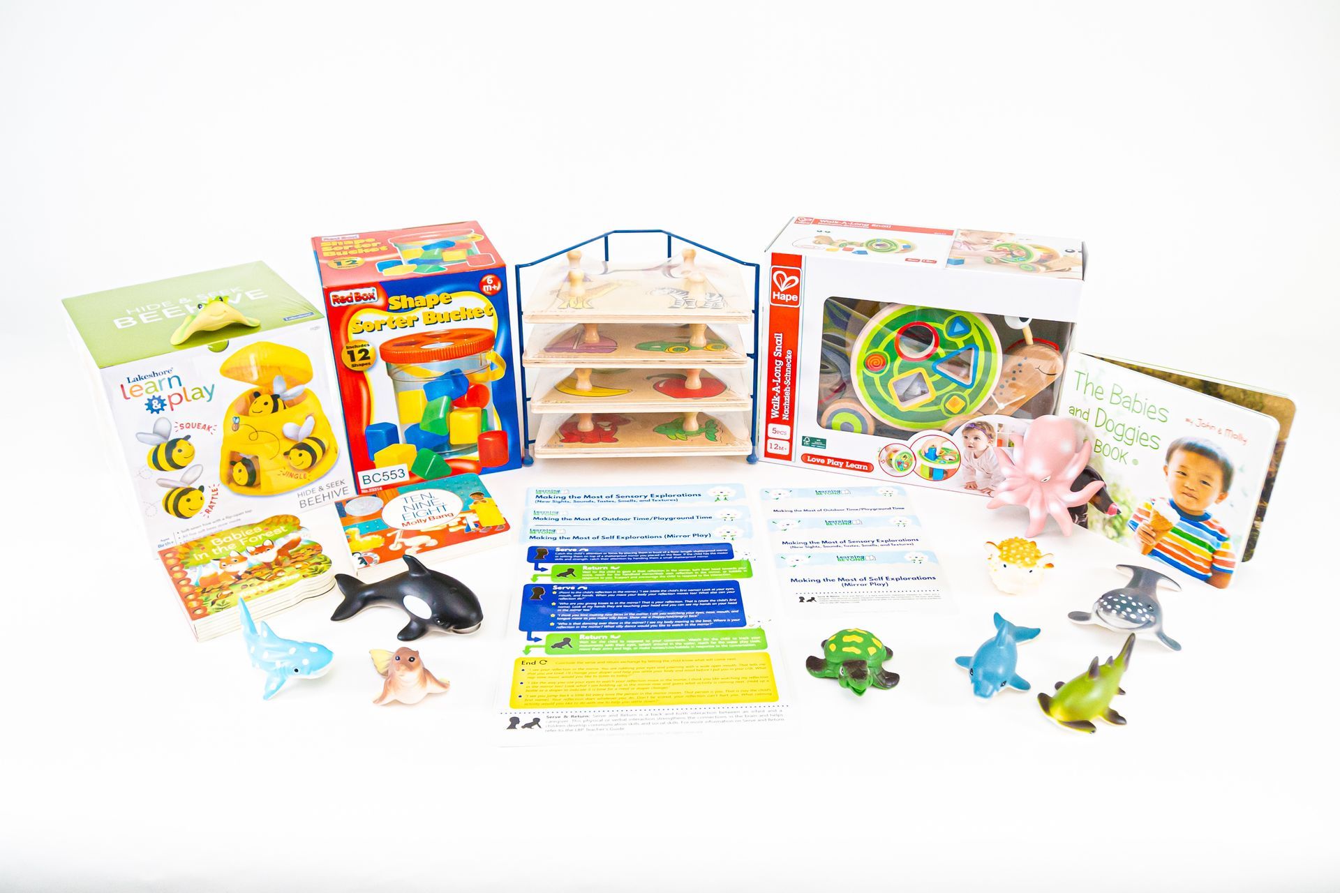 Assorted children's toys, including blocks, books, animal figurines, and a magnetic maze, laid out on a white surface.