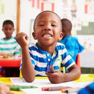 A young boy in a blue and white striped shirt is smiling while sitting at a table