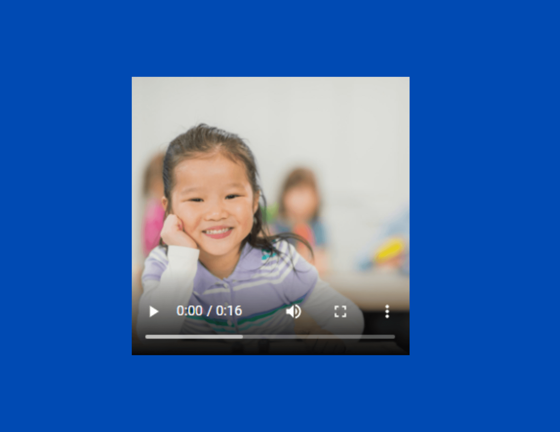 Smiling Asian girl in a classroom, watching a video, her face resting on her hand. Other students blurred in the background.
