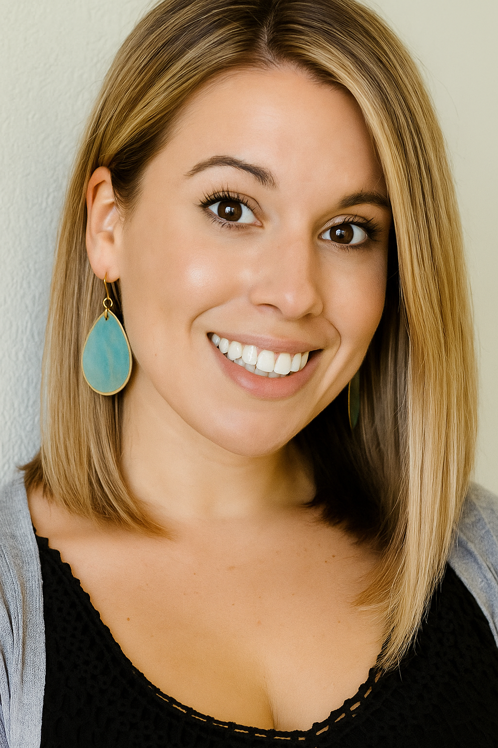 A woman in a black dress is smiling and leaning against a wall.