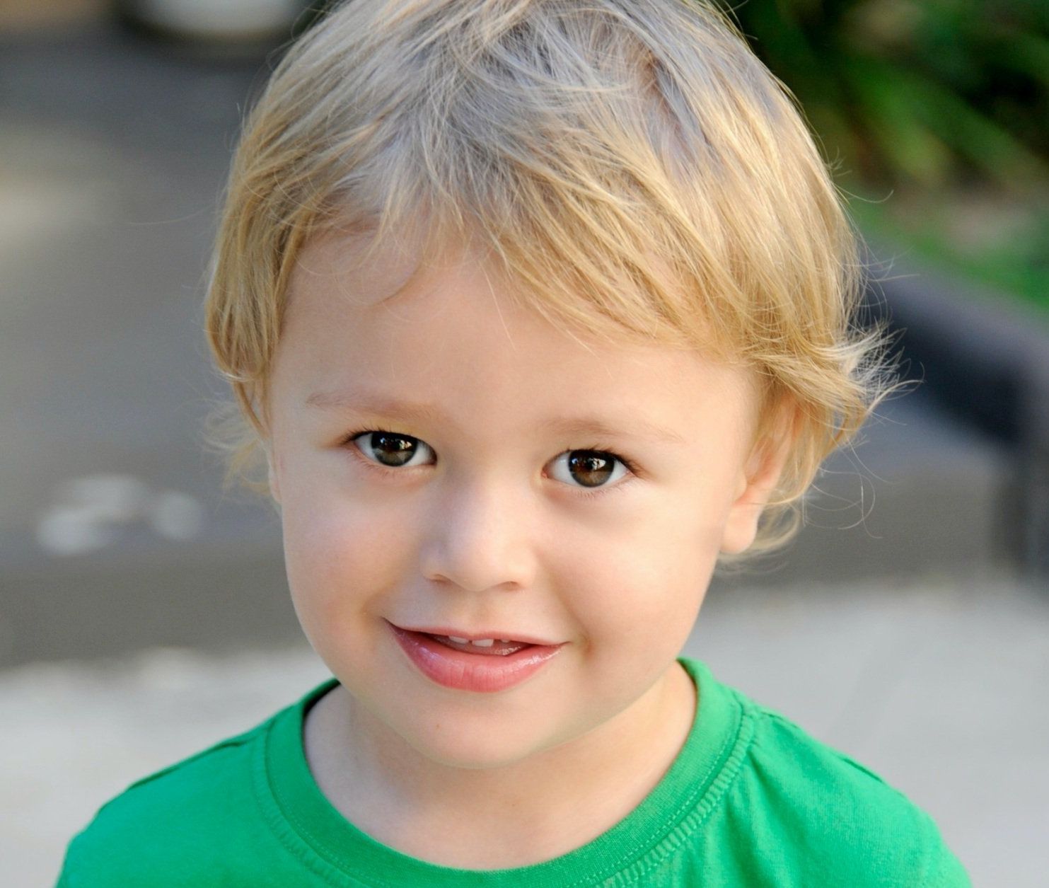 A little boy with blonde hair is wearing a green shirt