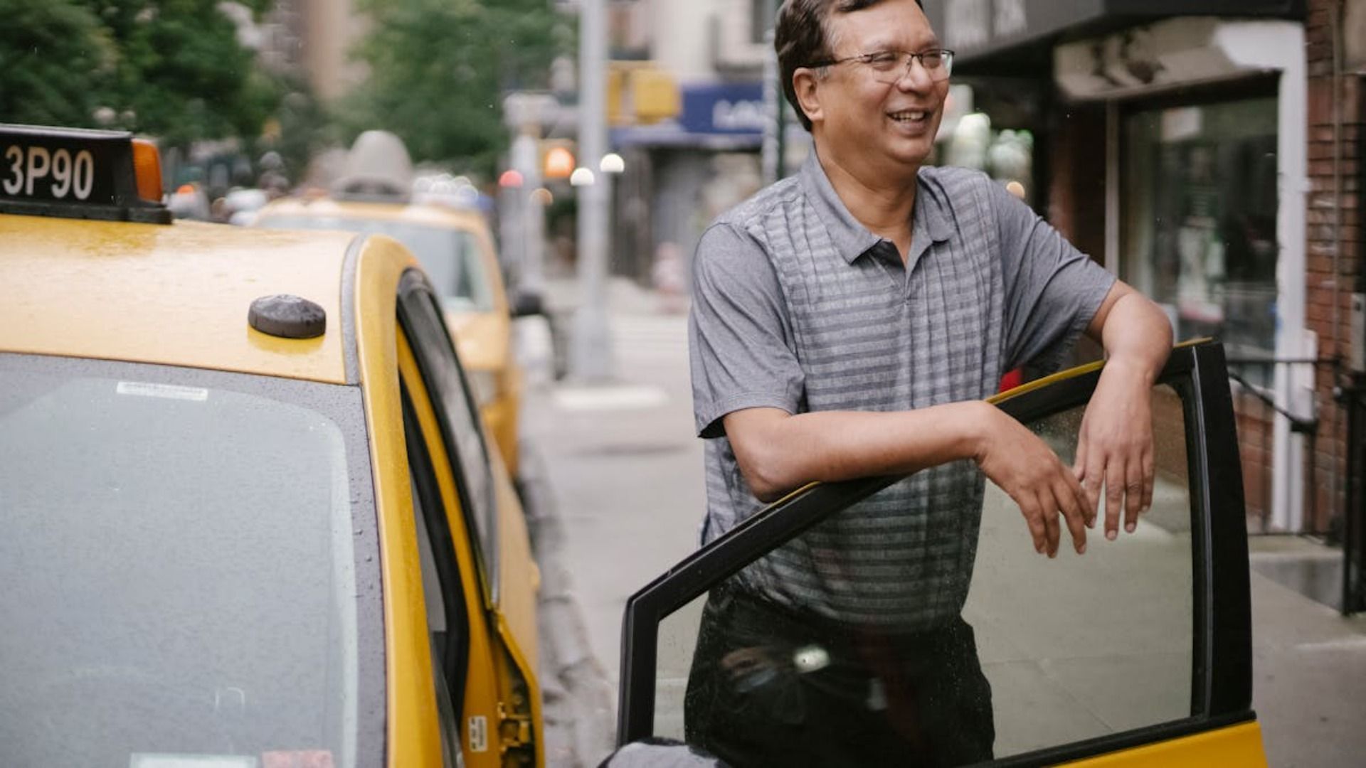 El hombre se apoya en la puerta abierta de un taxi en una calle de la ciudad, sonriendo.
