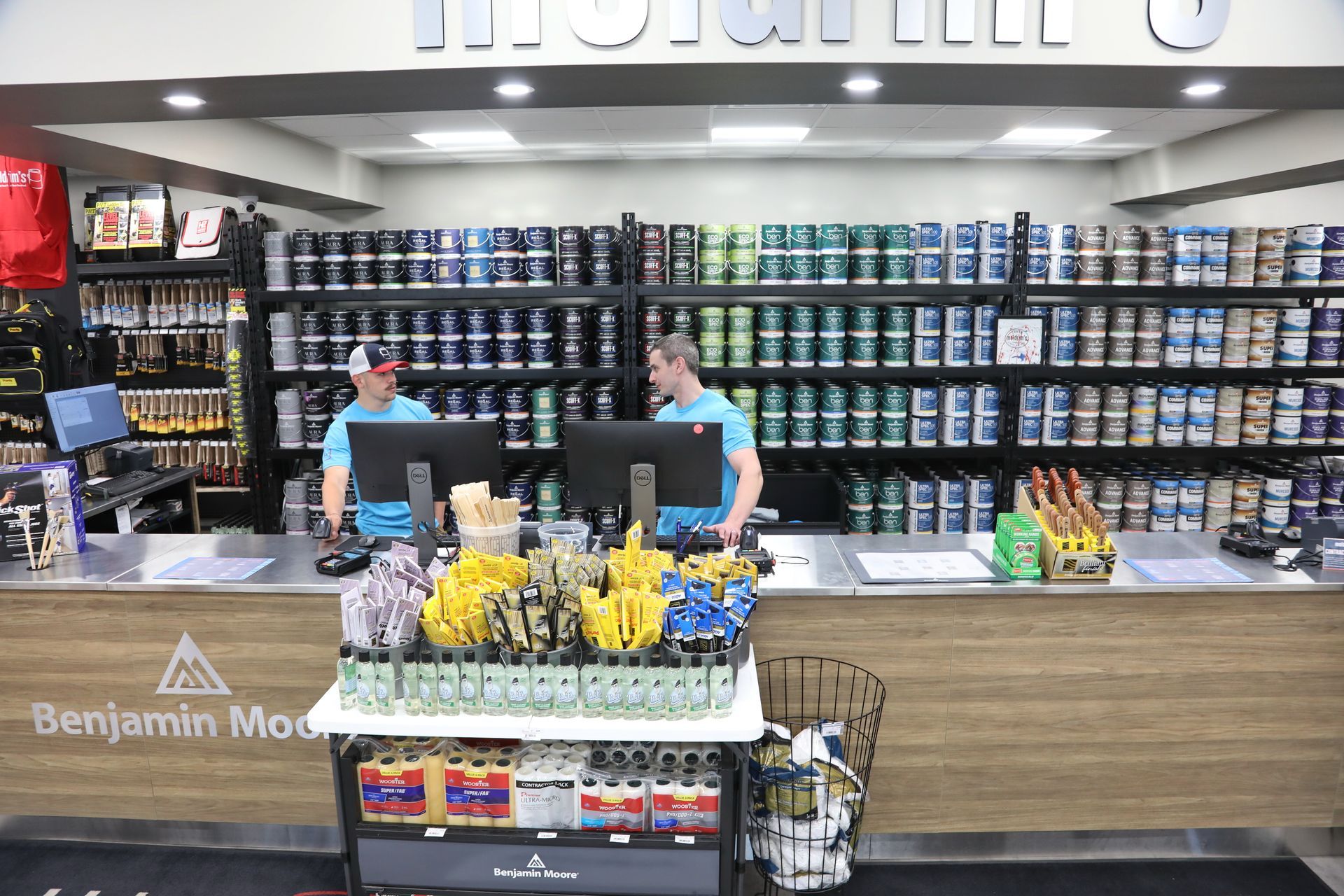 Two men are standing at a counter in a paint store.