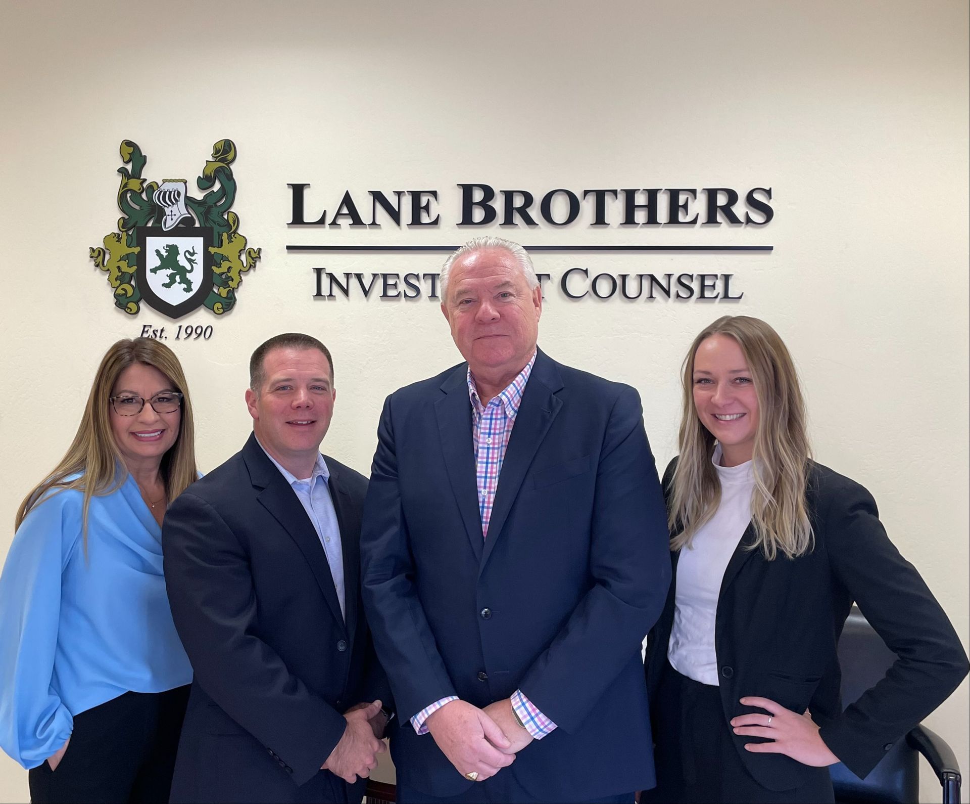 A group of people are posing for a picture in front of a wall that says lane brothers invest and counsel.