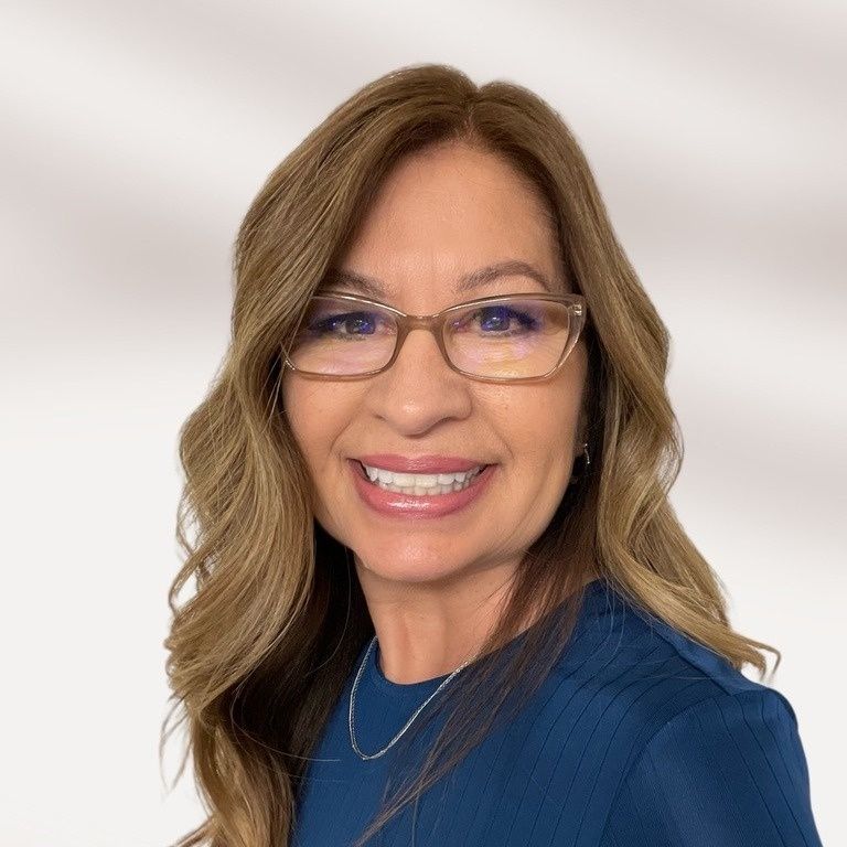 A woman wearing glasses and a blue shirt is smiling for the camera.
