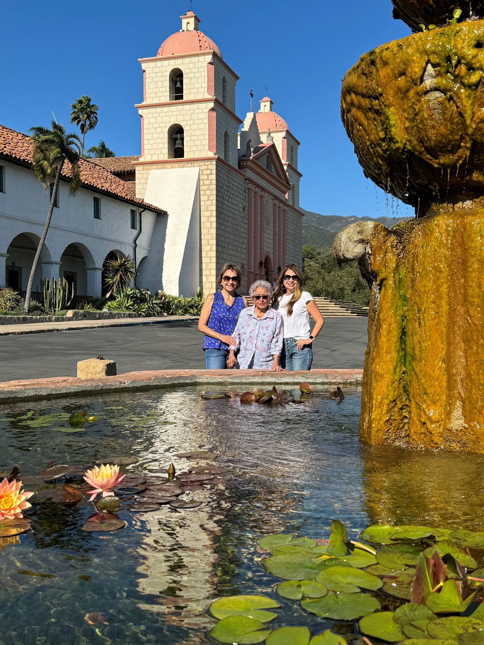 Three people standing next to a fountain in front of a church