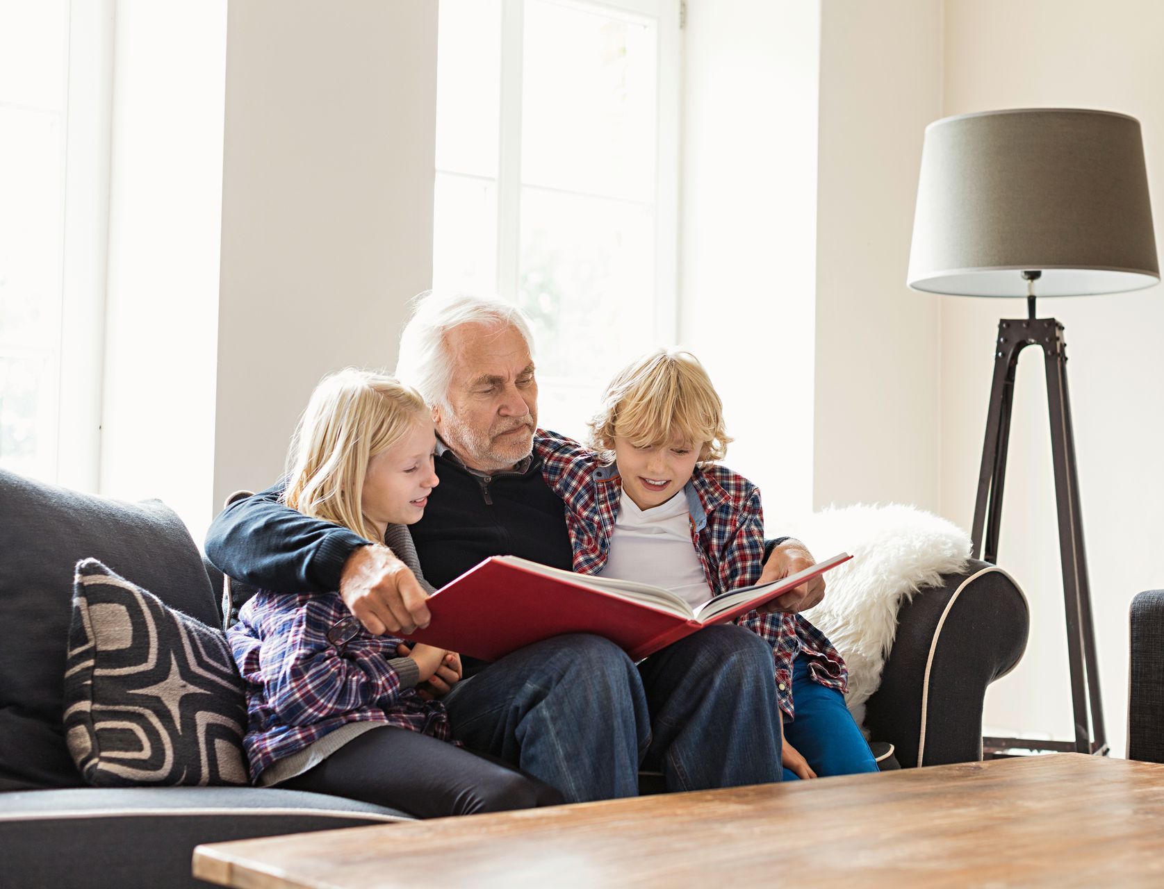 A man and two children are sitting on a couch reading a book.