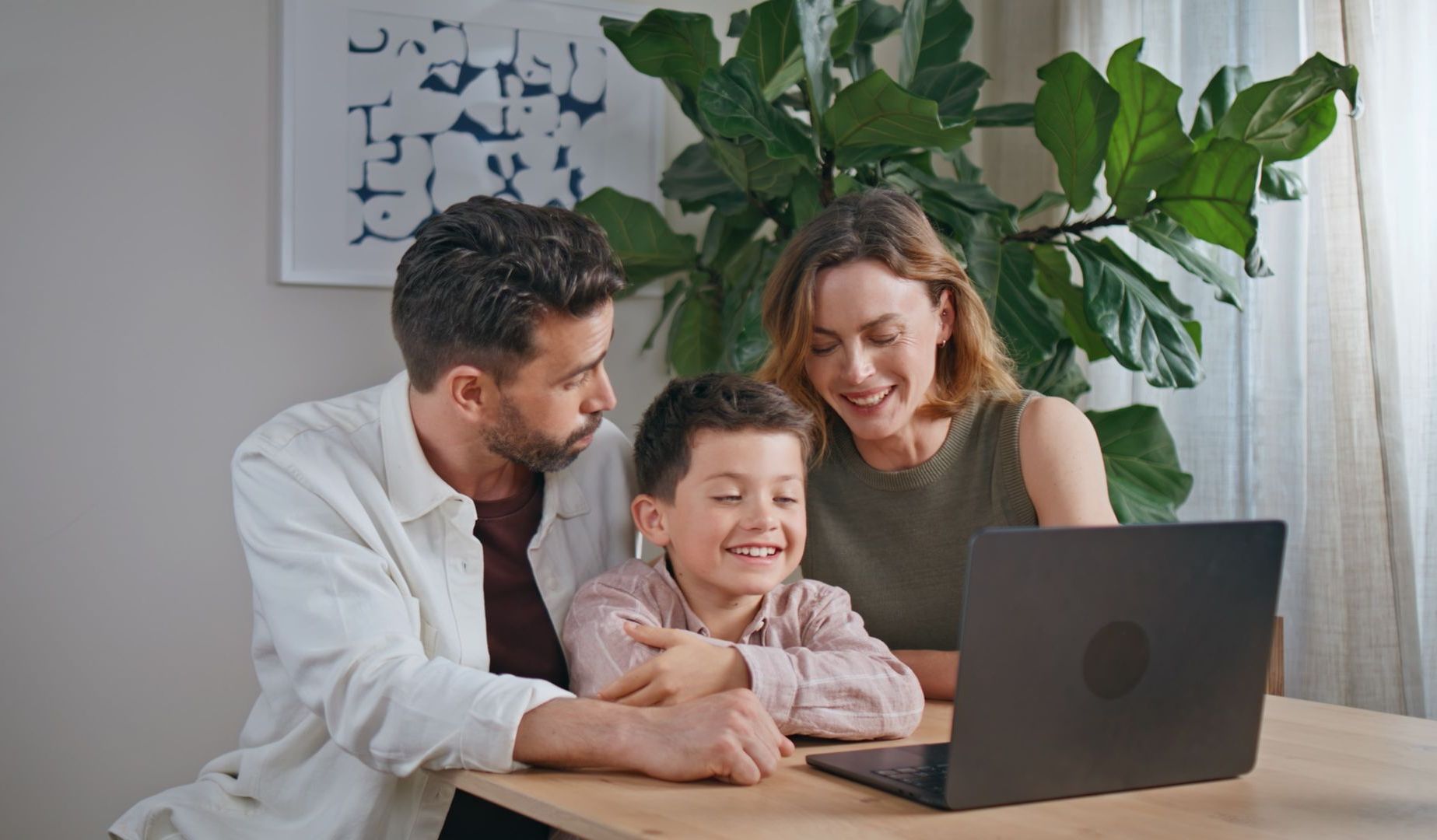 A family is sitting at a table looking at a laptop computer.