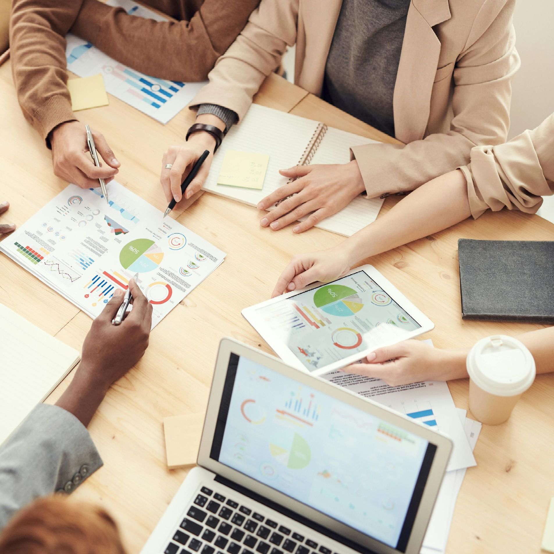 A group of people are sitting around a table with a laptop and papers