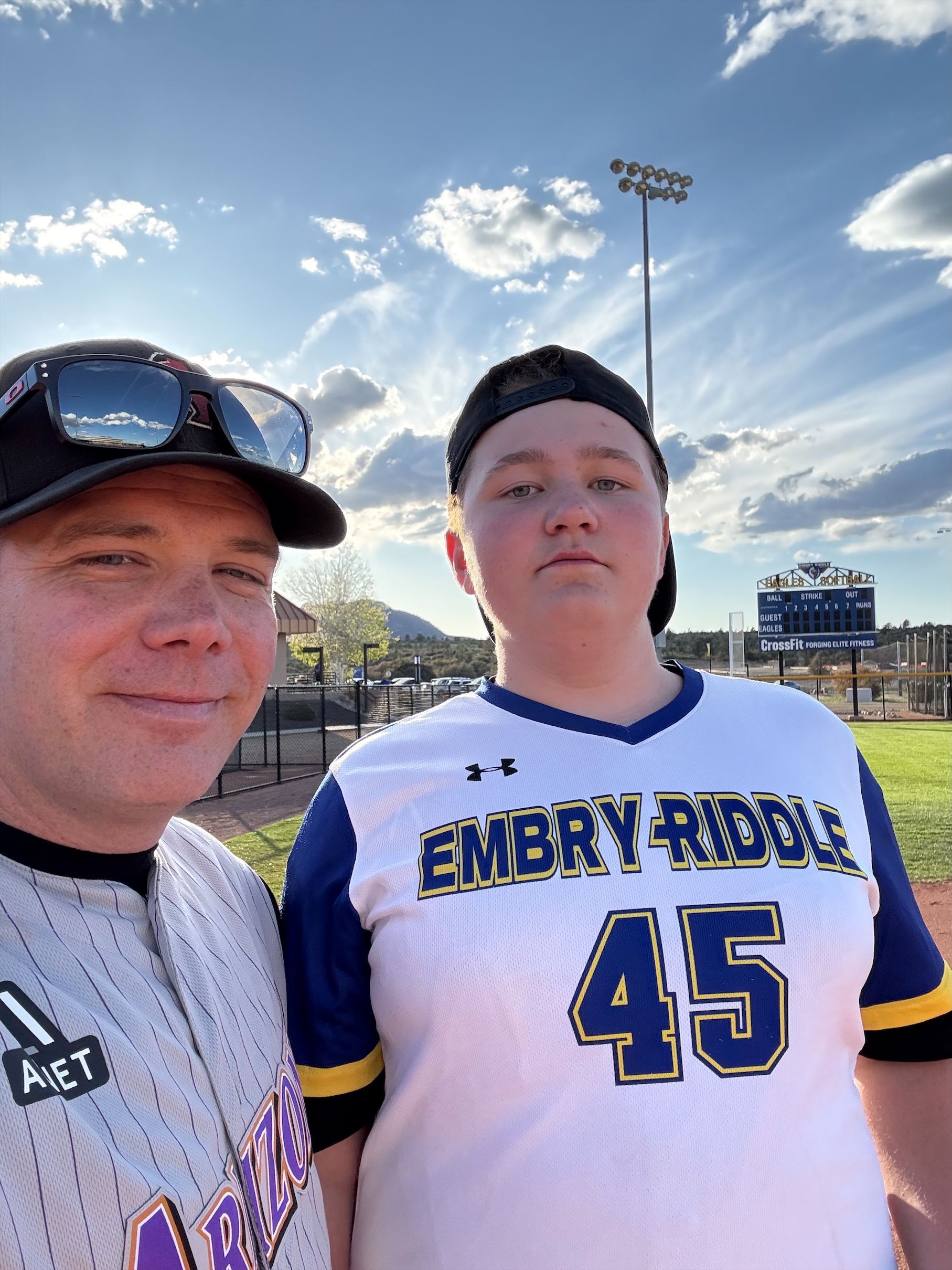 A man and a boy are standing next to each other on a baseball field.