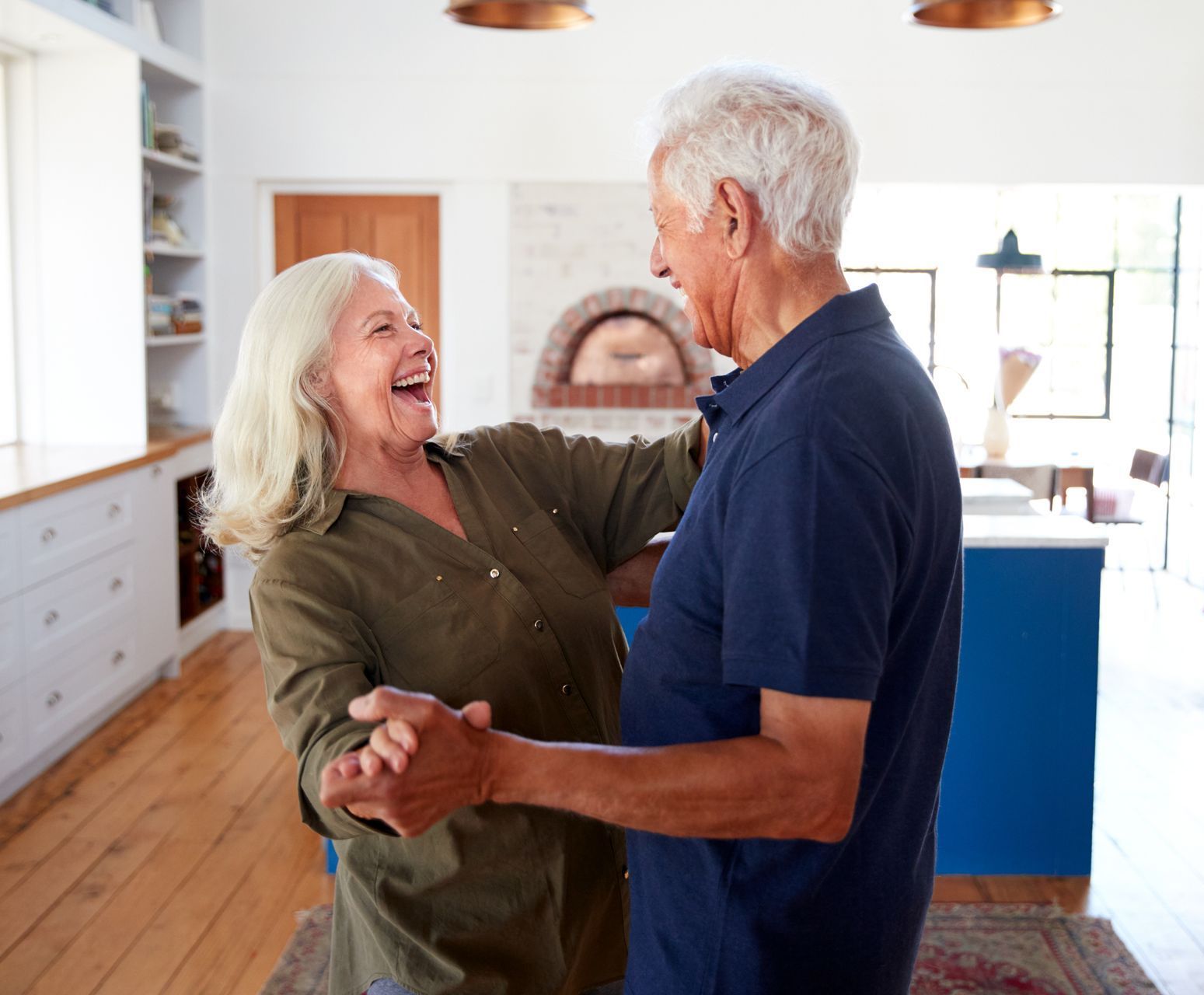 An elderly couple is dancing together in a living room.