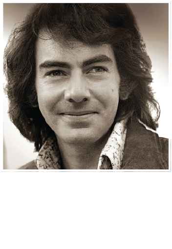 A black-and-white portrait of singer-songwriter Neil Diamond smiling softly while wearing a patterned collared shirt.
