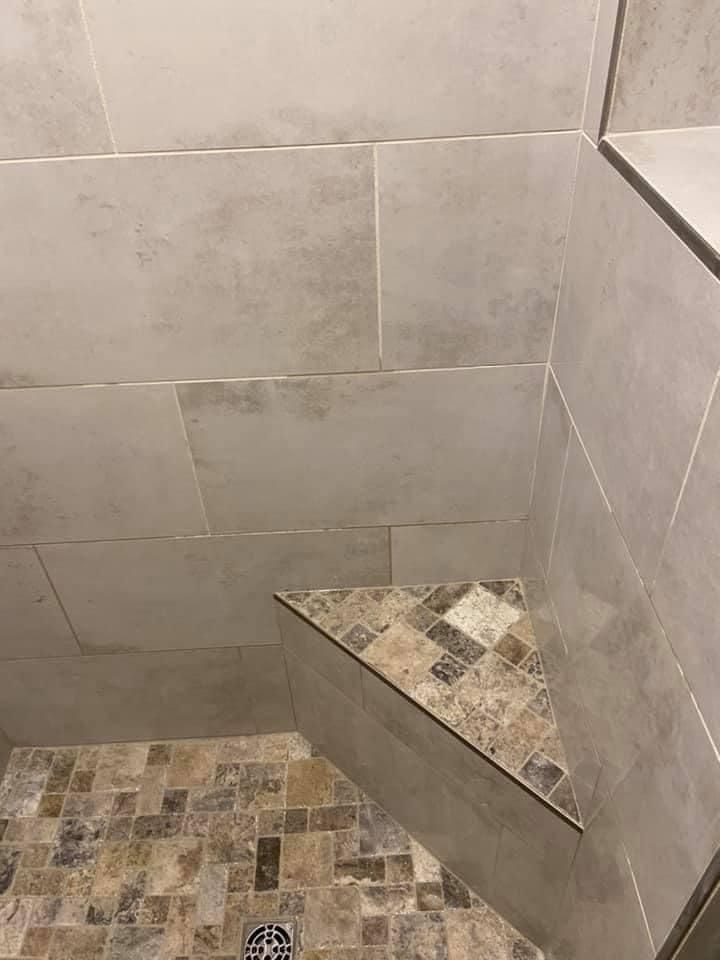A shower stall with a corner shelf and a drain.