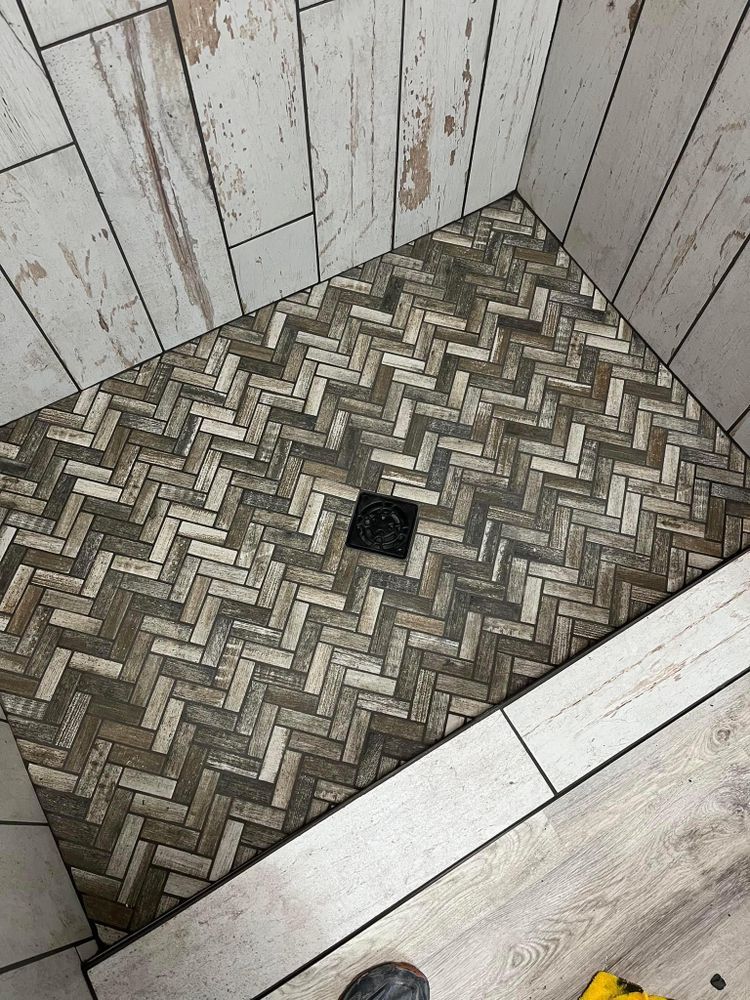 A walk in shower with a herringbone tile floor.