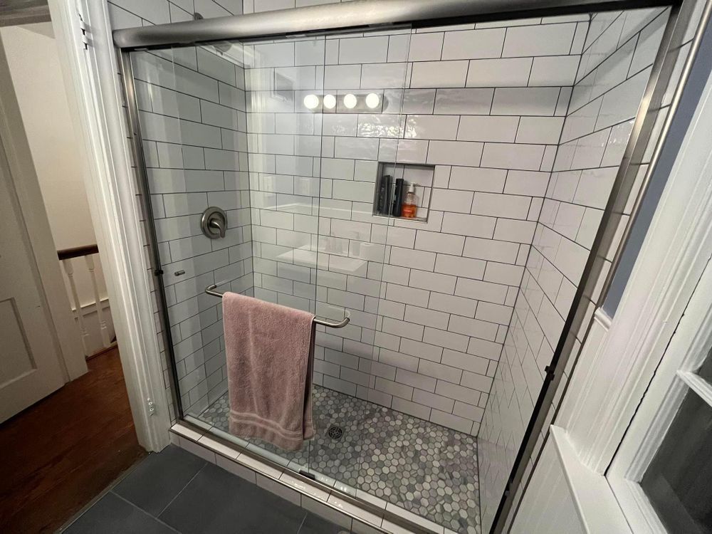 A bathroom with white brick walls and a walk in shower with a glass door.