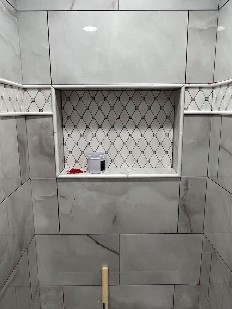 A bathroom with gray tiles and a shelf in the shower.
