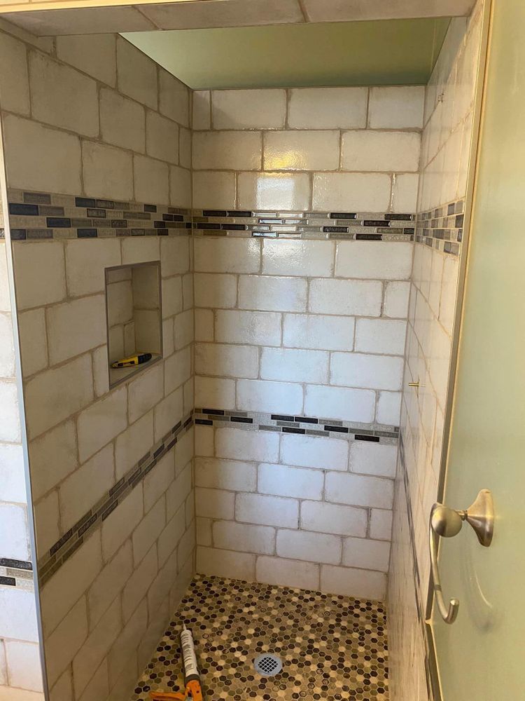 A bathroom shower with white tiles and a mosaic floor.