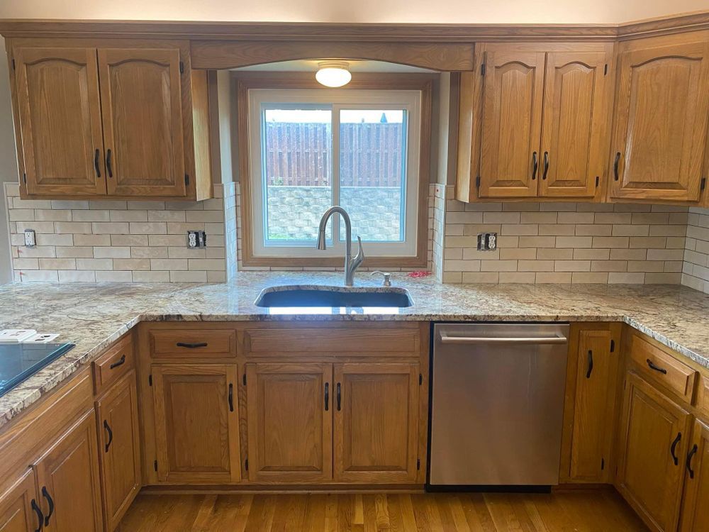 A kitchen with wooden cabinets , granite counter tops , a sink and a dishwasher.